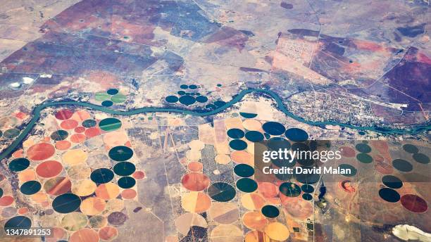 arial image of crop circles along a river with a small farming town. - arial desert stock pictures, royalty-free photos & images