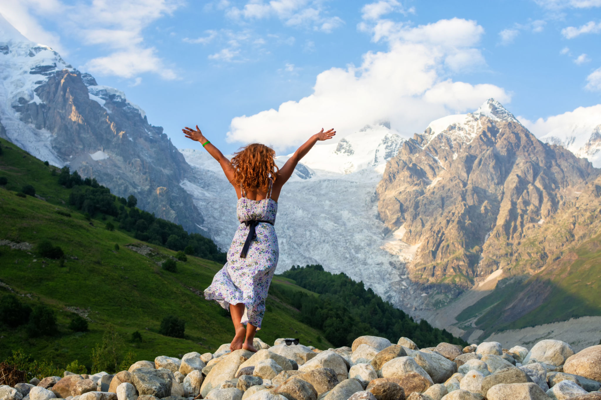 Young beautiful girl in a dress with red hair on the background of the Adishi glacier. Adish Glacier in Svaneti and the Caucasus Mountains. Young beautiful girl in a dress with red hair on the background of the Adishi glacier. Adish Glacier in Svaneti and the Caucasus Mountains.