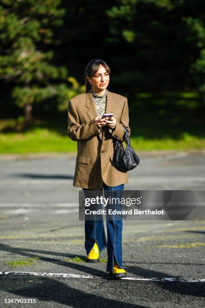 Guest wears gold earrings, a black with green / yellow flower print pattern turtleneck pullover, a brown and dark brown checkered print pattern...