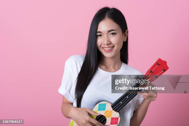 happy girl with ukulele in her hands stands on pink background, smiling girl musician plays ukulele. isolated. - ukulele stock-fotos und bilder