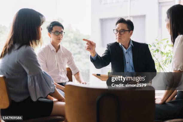 perplexed young asian woman looking at her leader pointing fingers at her - preconceito imagens e fotografias de stock
