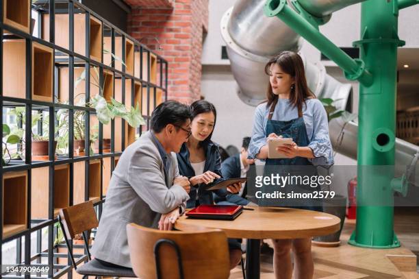 smiling small business coffee shop owner woman hold notepad take order serving couple customers - chinese waiter stock pictures, royalty-free photos & images