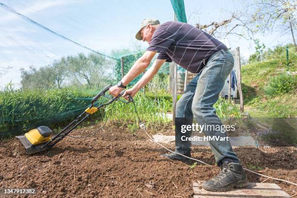 joyful mature man in springtime plowing the vegetable garden with an electric tiller -cultivator - harrow agricultural equipment stock pictures, royalty-free photos & images