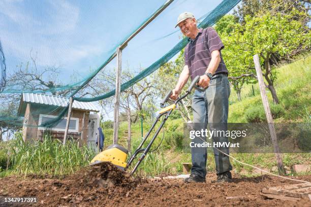 joyful mature man in springtime plowing the vegetable garden with an electric tiller -cultivator - harrow agricultural equipment stock pictures, royalty-free photos & images