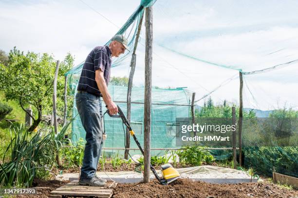 hombre maduro alegre en primavera arando el huerto con un cultivador eléctrico - harrow fotografías e imágenes de stock