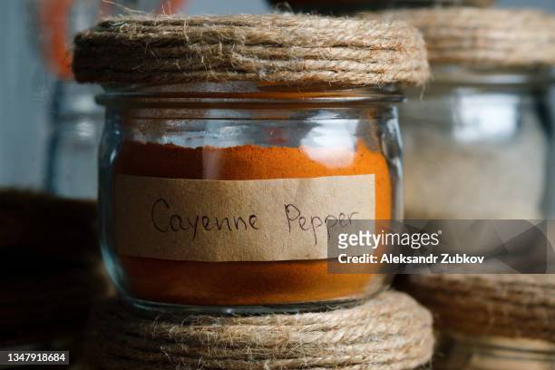 a composition of many different spices and herbs standing in a row on a wooden table or shelf. dry crushed spices and seasonings in glass jars and containers with inscriptions, in the kitchen cabinet or pantry. the concept of cooking, home decor. - cayenne ストックフォトと画像