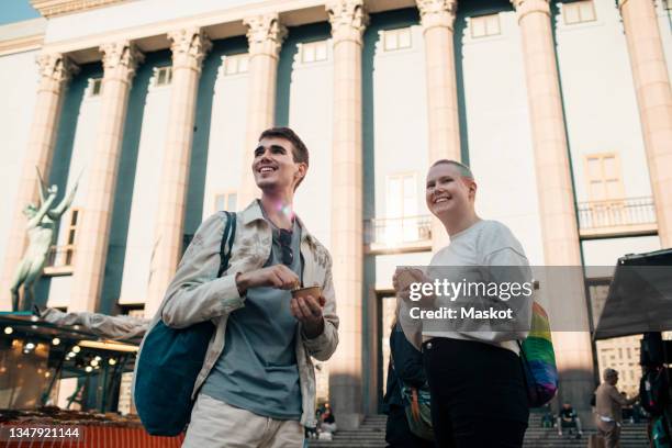 low angle view of young male friends with ice cream cups against building in city - ice cream cup stock-fotos und bilder