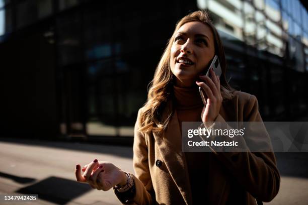 woman talking on a smart phone as she's walk to work - business woman looking over shoulder stock pictures, royalty-free photos & images