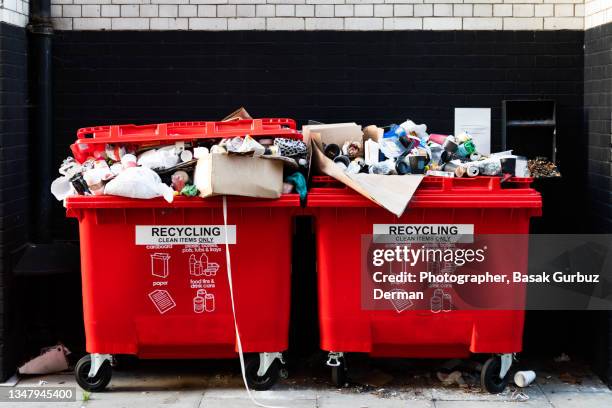 red recycling bins overflowing with rubbish on the street. - müllcontainer stock-fotos und bilder