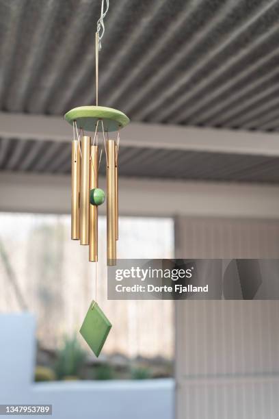 green and golden wind chime in wood and metal with a blurred background - campana fotografías e imágenes de stock