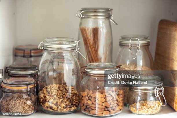 looking into a kitchen cupboard containing cereals, nuts, seeds and pasta in glass jars with lids - jarra recipiente - fotografias e filmes do acervo