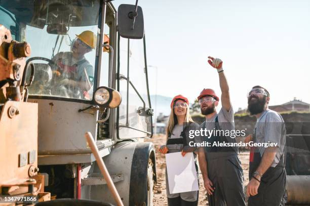 des ingénieurs civils et des travailleurs de la construction discutent de la procédure avec le conducteur du bulldozer - engin de chantier photos et images de collection
