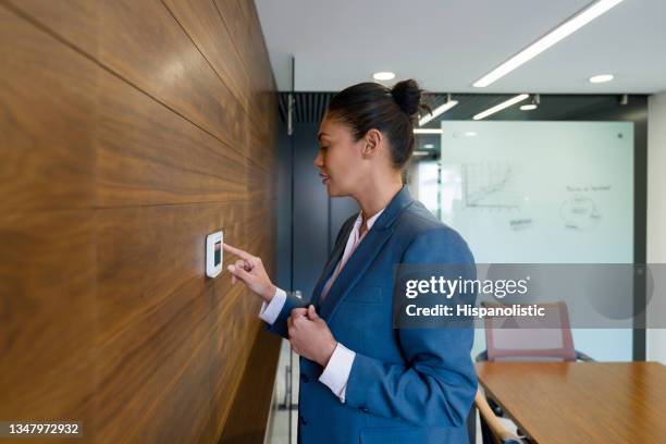 business woman adjusting the thermostat at the office - eficiência energética imagens e fotografias de stock