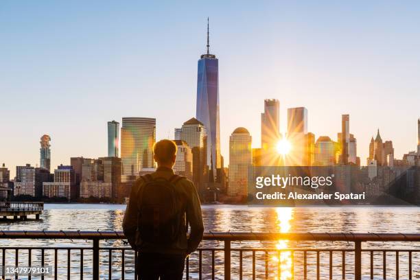man with backpack looking at new york skyline at sunrise, rear view - staat new york bildbanksfoton och bilder