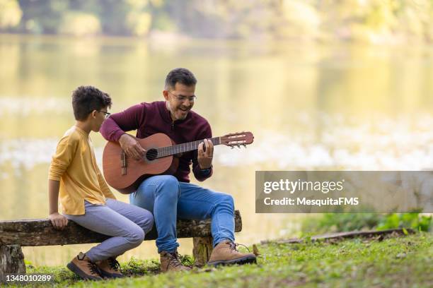 father and son playing guitar in front of the lake - father and son park stock pictures, royalty-free photos & images