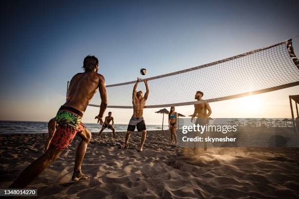 large group of friends playing beach volleyball at sunset. - beach volleyball group stock pictures, royalty-free photos & images