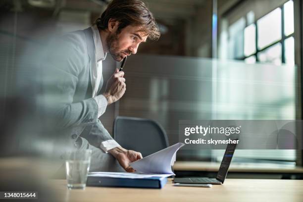 young businessman brainstorming while comparing data in the office. - examining paperwork stock pictures, royalty-free photos & images