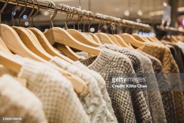 knit sweaters hanging on clothes rack in a store - barra para colgar la ropa fotografías e imágenes de stock