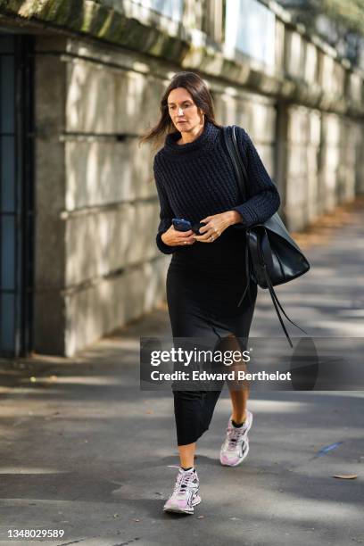 Guest wears a black wool pullover, a black long slit / split dress, a black shiny leather large shoulder bag, silver rings, white and pale pink...