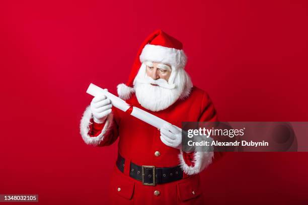 portrait of santa claus with letter of wishes for gifts on red background with copy space. new year concept - santa beard stock pictures, royalty-free photos & images