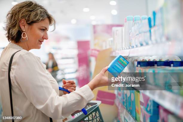 mujer eligiendo toallas sanitarias en el supermercado - pasillo objeto fabricado fotografías e imágenes de stock