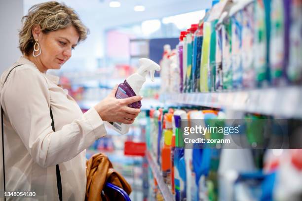 woman choosing domestic cleaning product by the supermarket shelf - städutrustning bildbanksfoton och bilder