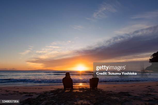 a couple watching the sunrise on a beach on vacation. - japan sunrise stock-fotos und bilder