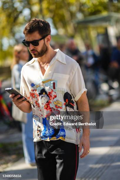Guest wears sunglasses, a white shirt with multicolored Japanese drawings short sleeves shirt, black with red sides stripes pants, outside Rick...