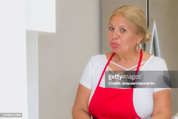 latin mature woman cooking christmas dinner / thanksgiving dinner for christmas night / thanksgiving day inside in a latin moderm home in miami, united states wearing white shirt and a red apron after corona virus covid-19 pandemic illness breakdown. - virtual thanksgiving stock pictures, royalty-free photos & images