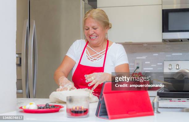 latin mature woman cooking christmas dinner / thanksgiving dinner for christmas night / thanksgiving day inside in a latin moderm home in miami, united states wearing white shirt and a red apron after corona virus covid-19 pandemic illness breakdown. - virtual thanksgiving stock pictures, royalty-free photos & images