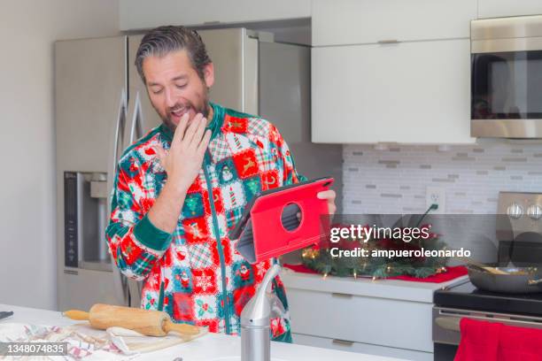 latin young man cooking christmas dinner / thanksgiving dinner for christmas night / thanksgiving day inside in a latin moderm home in miami, united states wearing a christmas shirt / pajamas corona virus covid-19 pandemic illness breakdown. - christmas zoom stock pictures, royalty-free photos & images
