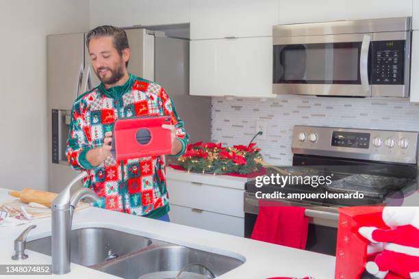 latin young man cooking christmas dinner / thanksgiving dinner for christmas night / thanksgiving day inside in a latin moderm home in miami, united states wearing a christmas shirt / pajamas corona virus covid-19 pandemic illness breakdown. - virtual thanksgiving stock pictures, royalty-free photos & images