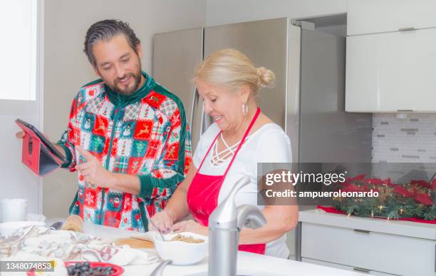 latin mature woman cooking christmas dinner / thanksgiving dinner for christmas night / thanksgiving day with her son, inside in a latin moderm home in miami, united states wearing white shirt, red apron and christmas pajamas. - virtual thanksgiving stock pictures, royalty-free photos & images