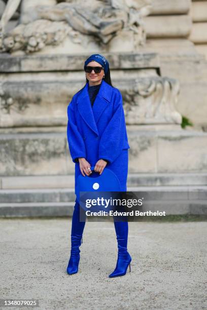 Guest wears a royal blue with brown and white print pattern silk scarf in the hair, black sunglasses, earrings, a navy blue sequined high neck...