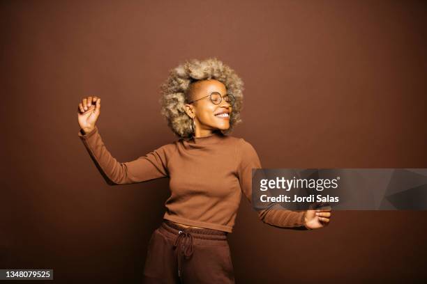 woman dancing against a brown background - afro frisur stock-fotos und bilder