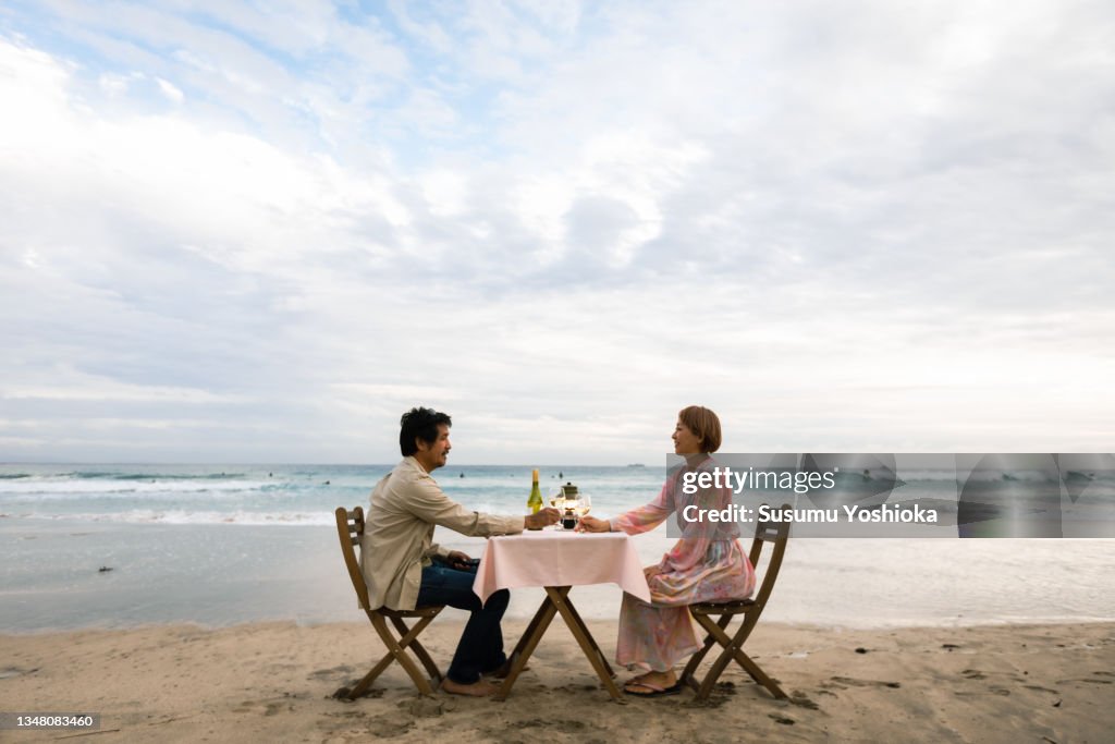 A couple enjoying a glass of wine while looking out at the ocean on a beautiful beach in the evening.