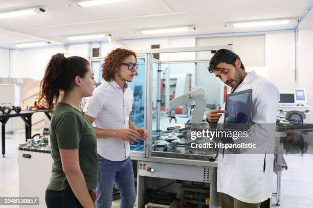 teacher explaining something to a couple of college students in a robotics class - school building stockfoto's en -beelden