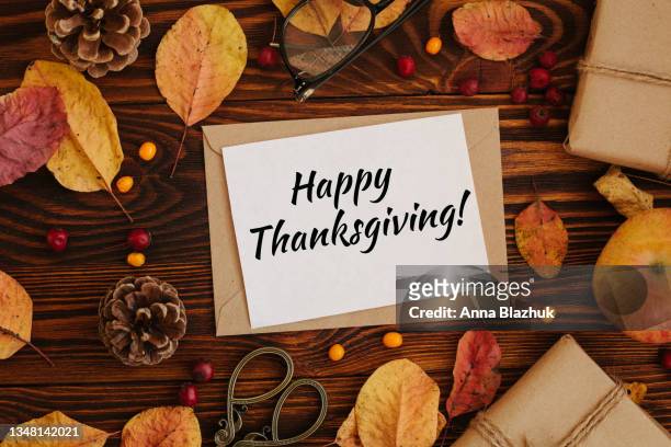 greeting card for thanksgiving day. brown table with apples, yellow autumn trees, pine cones and gift boxes and paper with text happy thanksgiving! - thanksgiving greeting stock pictures, royalty-free photos & images