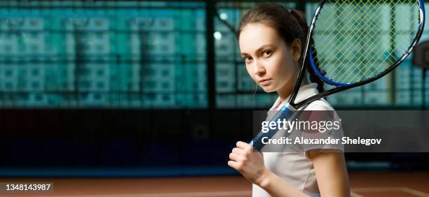 beautiful young woman posing on tennis court. female fashion portrait with tennis player indoors, girl wearing sports outfit. person is holding and using racket for game, lifestyle concept with people - hit face ball stock pictures, royalty-free photos & images