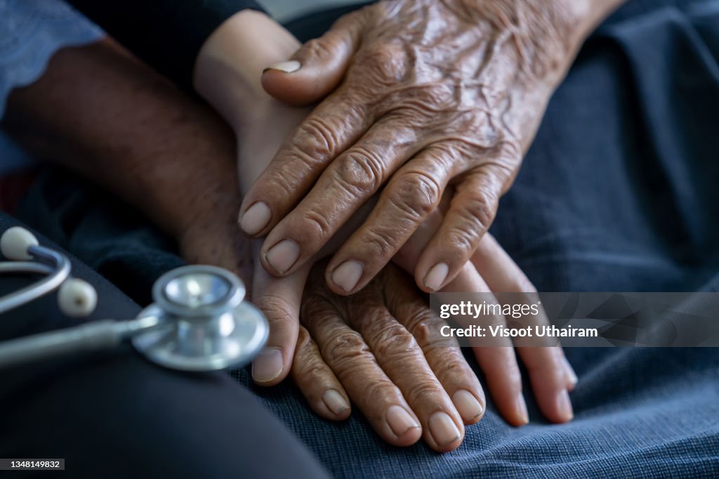 Close up of young nurse holding old man's hands and encourage him.