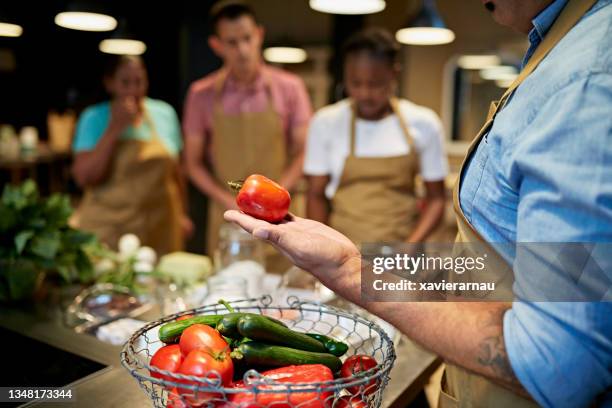 man holding plum tomato in team cooking class - basket universitario imagens e fotografias de stock