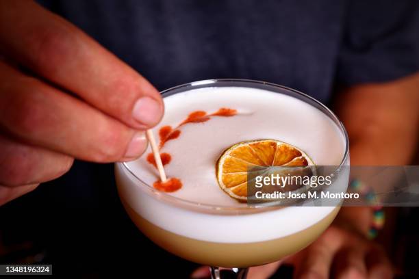 the barman finishes a pisco sour cocktail with a watermark on the foam of the drink. - pisco sour stockfoto's en -beelden