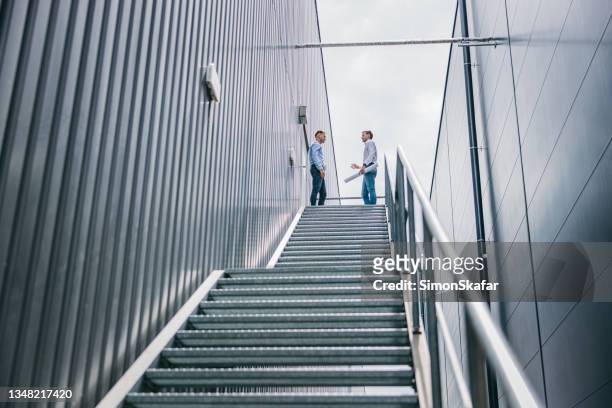 zwei ingenieure diskutieren im stehen auf der treppe - business man overseeing blueprints outdoor stock-fotos und bilder