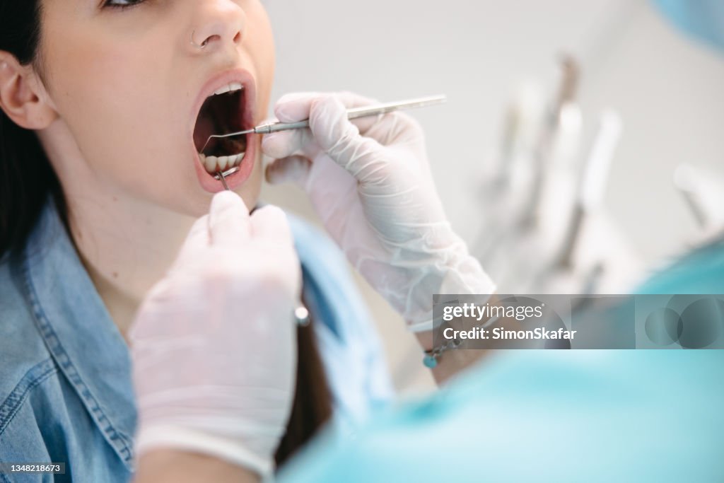 Feche acima da mão do dentista examinando os dentes da paciente do sexo feminino