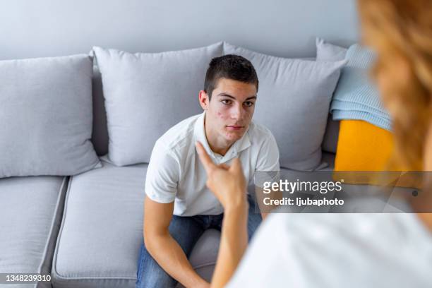 mature mother and her teenage son arguing at home while sitting on sofa. - angry boy stockfoto's en -beelden