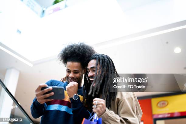brothers watching sports or playing on the smartphone at the mall - football phone stock pictures, royalty-free photos & images