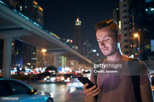 man using phone on city street at night - dubai taxi foto e immagini stock