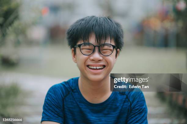 asian chinese teenage boy with eyeglasses looking at camera smiling at backyard of house outdoor - chinese teenage boy stockfoto's en -beelden