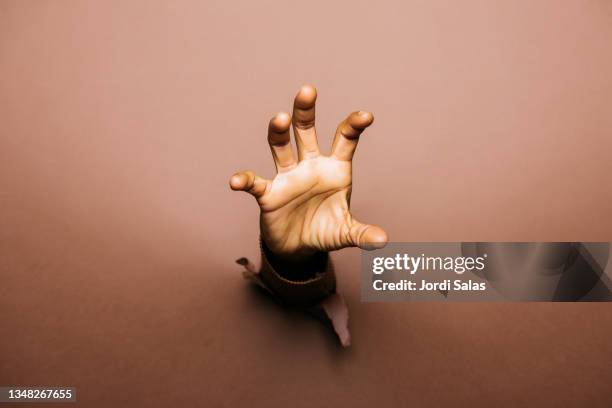 hand of a person through a hole of a brown paper wall. - catching hands stock pictures, royalty-free photos & images