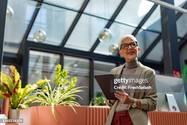 confident, happy senior businesswoman with short hair standing outside and holding a digital tablet - women's short program imagens e fotografias de stock